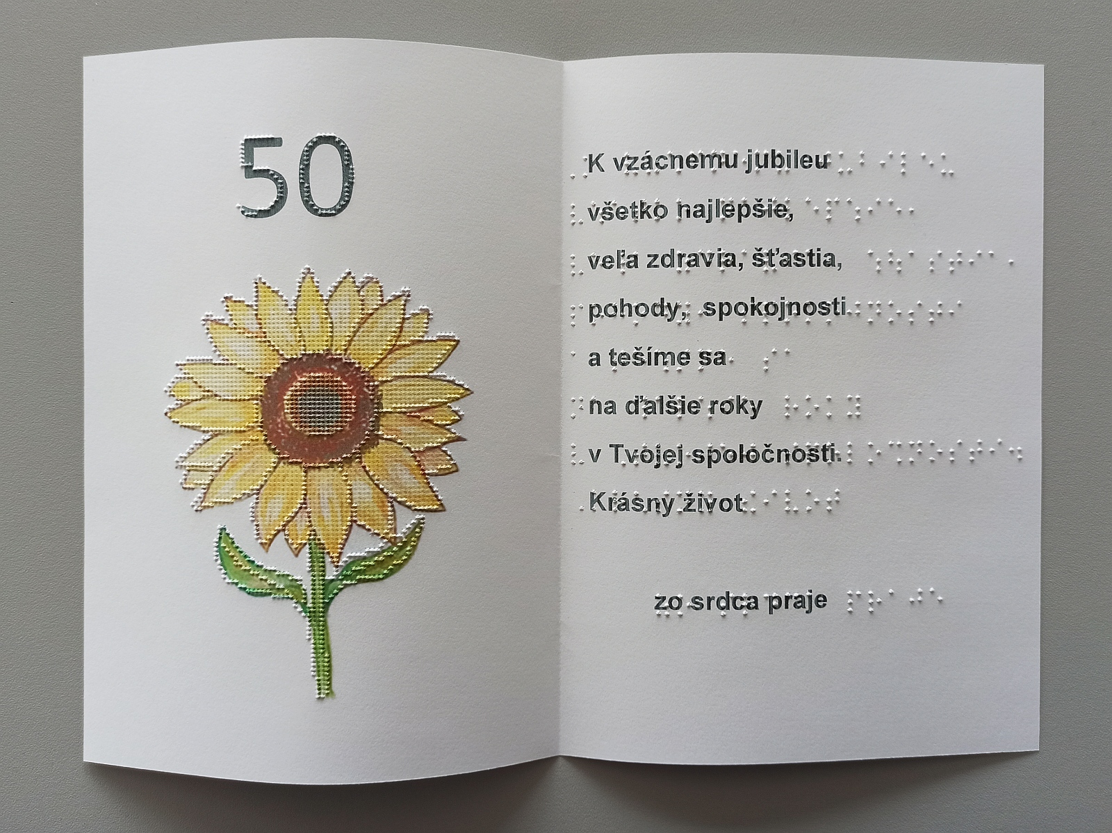 Fotografia pohľadnice v kombinácii brail/čiernotlač. Vybodkovaný obrázok kvetu slnečnice a text v čiernotlači aj braili.
